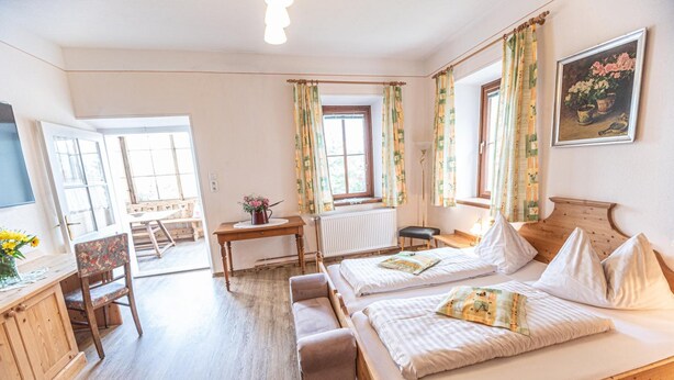 A cozy bedroom with a wooden bed, a desk, and a chair. There is a window with curtains, a radiator, and a painting on the wall. - Hotel Gasthof Gribelehof (Lienz)