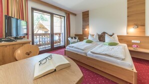 A hotel room with a bed, a desk, a television, and a view of the outside. - Hotel Gasthof Gribelehof (Lienz)