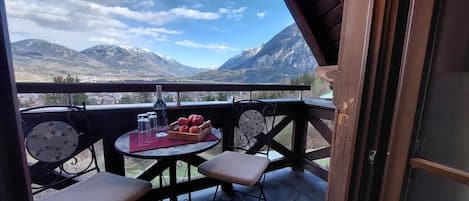 A balcony with a table, chairs, and a bottle of wine, overlooking a mountainous landscape.