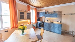 A modern kitchen with a wooden ceiling, a dining table with a vase of flowers, and a view of the outside. - Hotel Gasthof Gribelehof (Lienz)