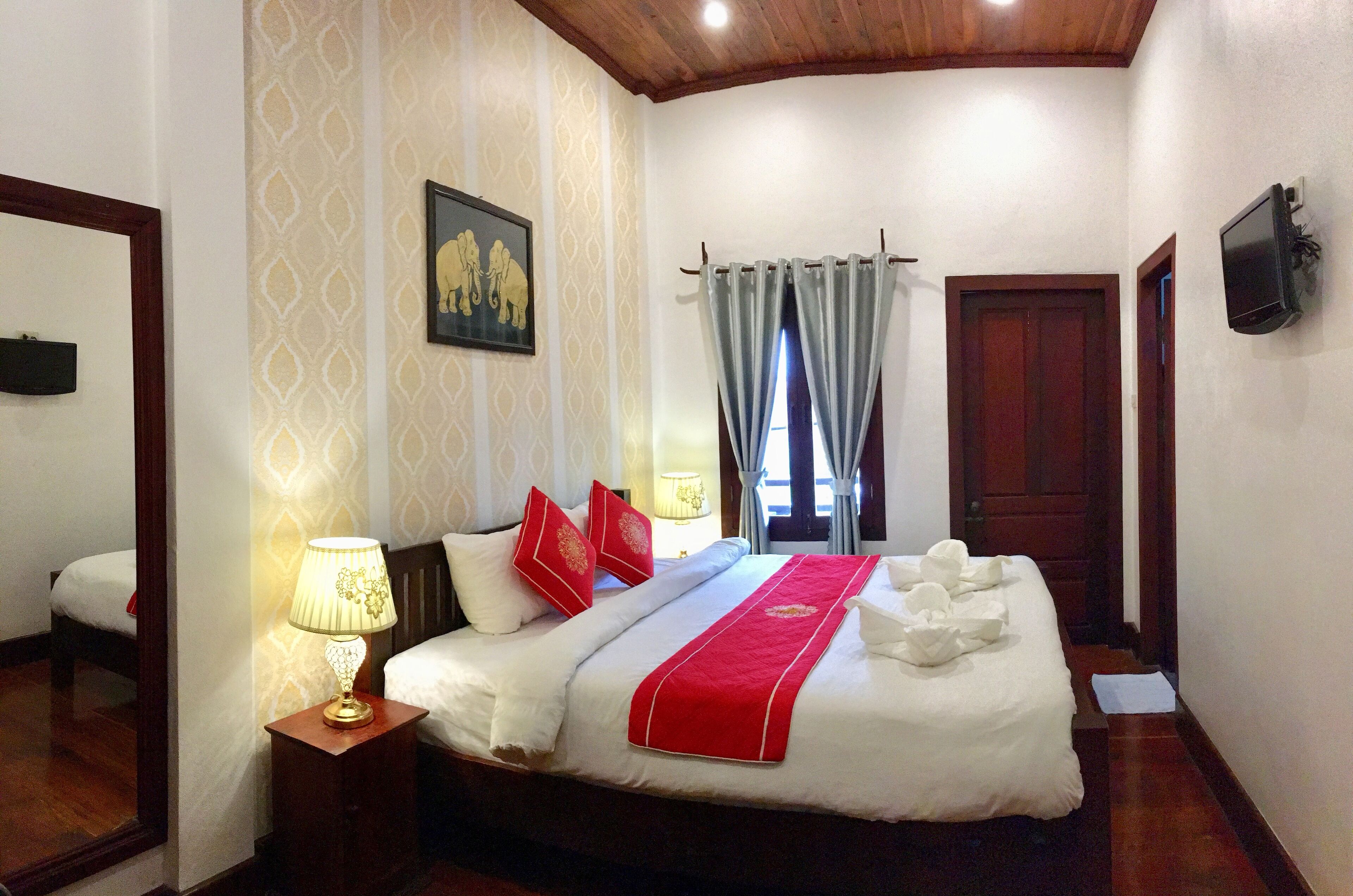 A hotel room with a large bed, a nightstand with a lamp, a painting on the wall, and a TV mounted on the wall.