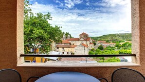 Un balcon offrant une vue sur une ville historique, avec notamment une église dotée d’un clocher, le tout entouré de verdure et de bâtiments.