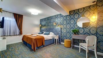 Habitación de hotel con cama, escritorio, silla, espejo redondo y una planta pequeña.