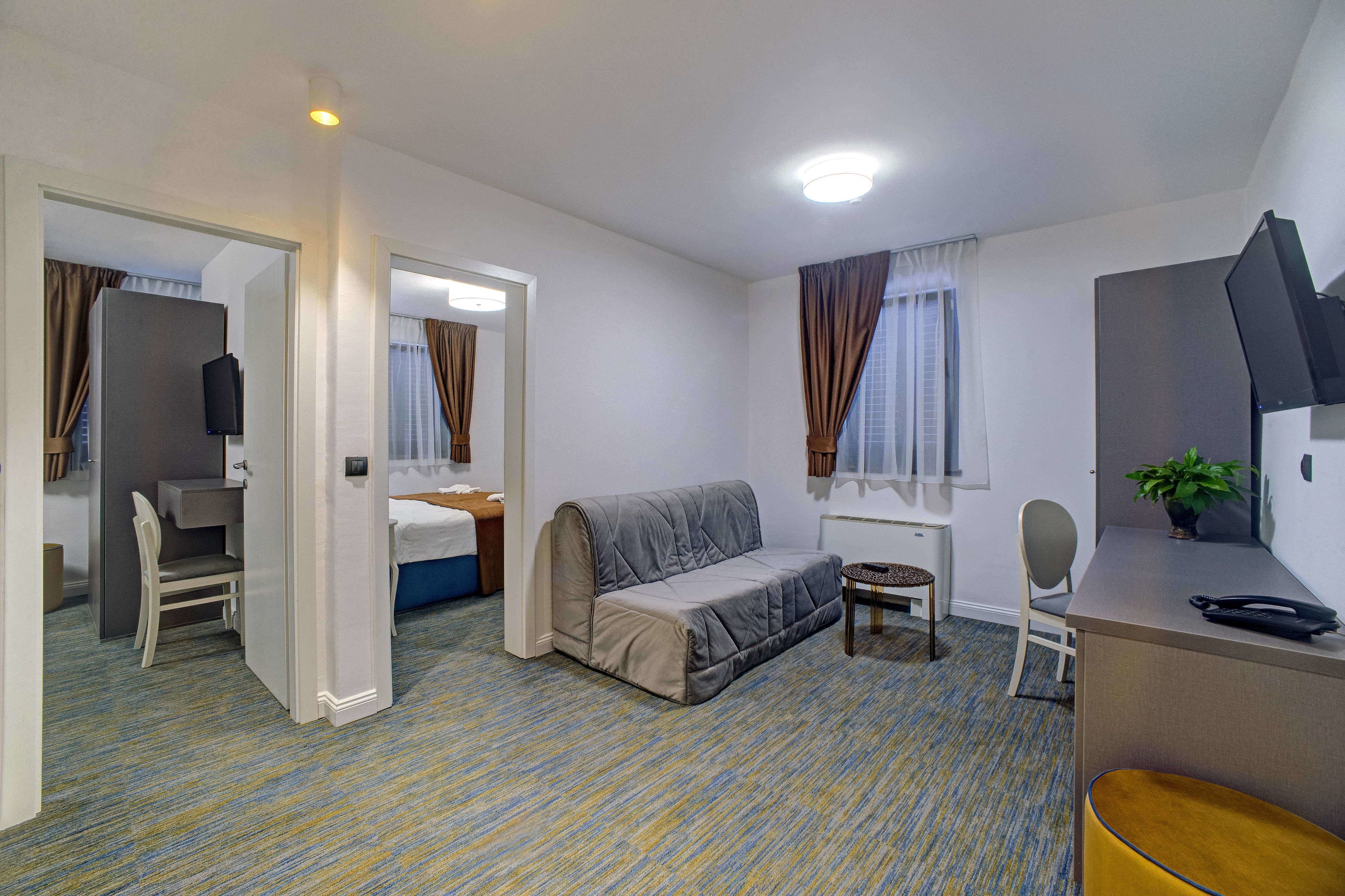 Una habitación de hotel compacta con cama, sofá, escritorio y silla.
