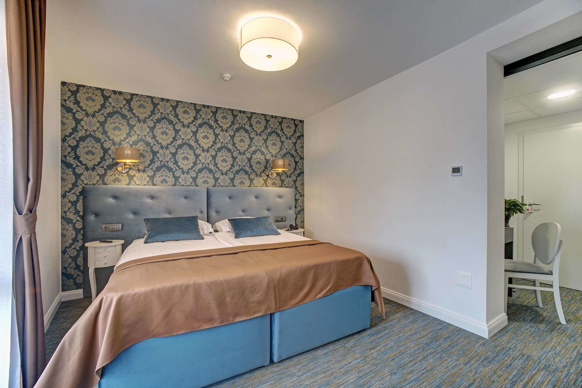 Une chambre d’hôtel avec un grand lit, deux tables de chevet, une tête de lit et un papier peint à motifs.