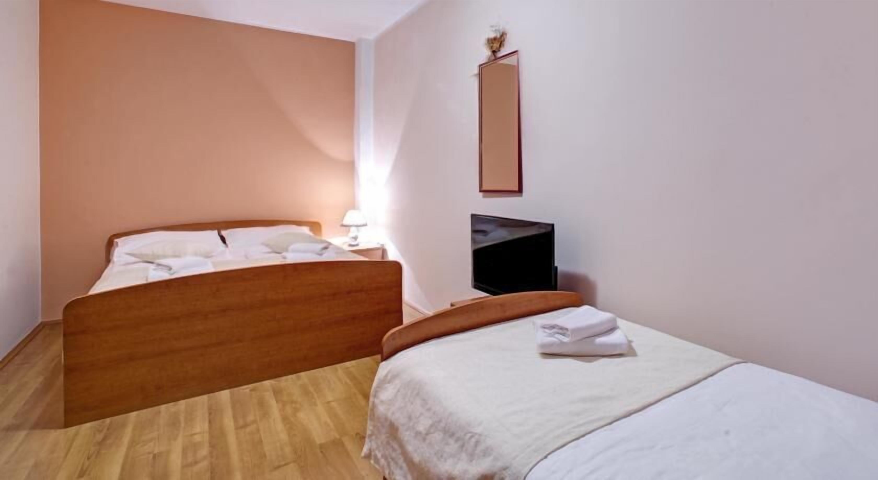 Ein Schlafzimmer mit zwei hölzernen Betten, einem Flachbildfernseher und einem Spiegel an der Wand.
