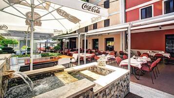 An outdoor dining area with tables and chairs, a stone fountain, and umbrellas with Coca-Cola branding.