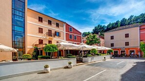 Une rue bordée de terrasses, un immeuble à la façade vitrée et un bâtiment rouge doté d’un balcon.
