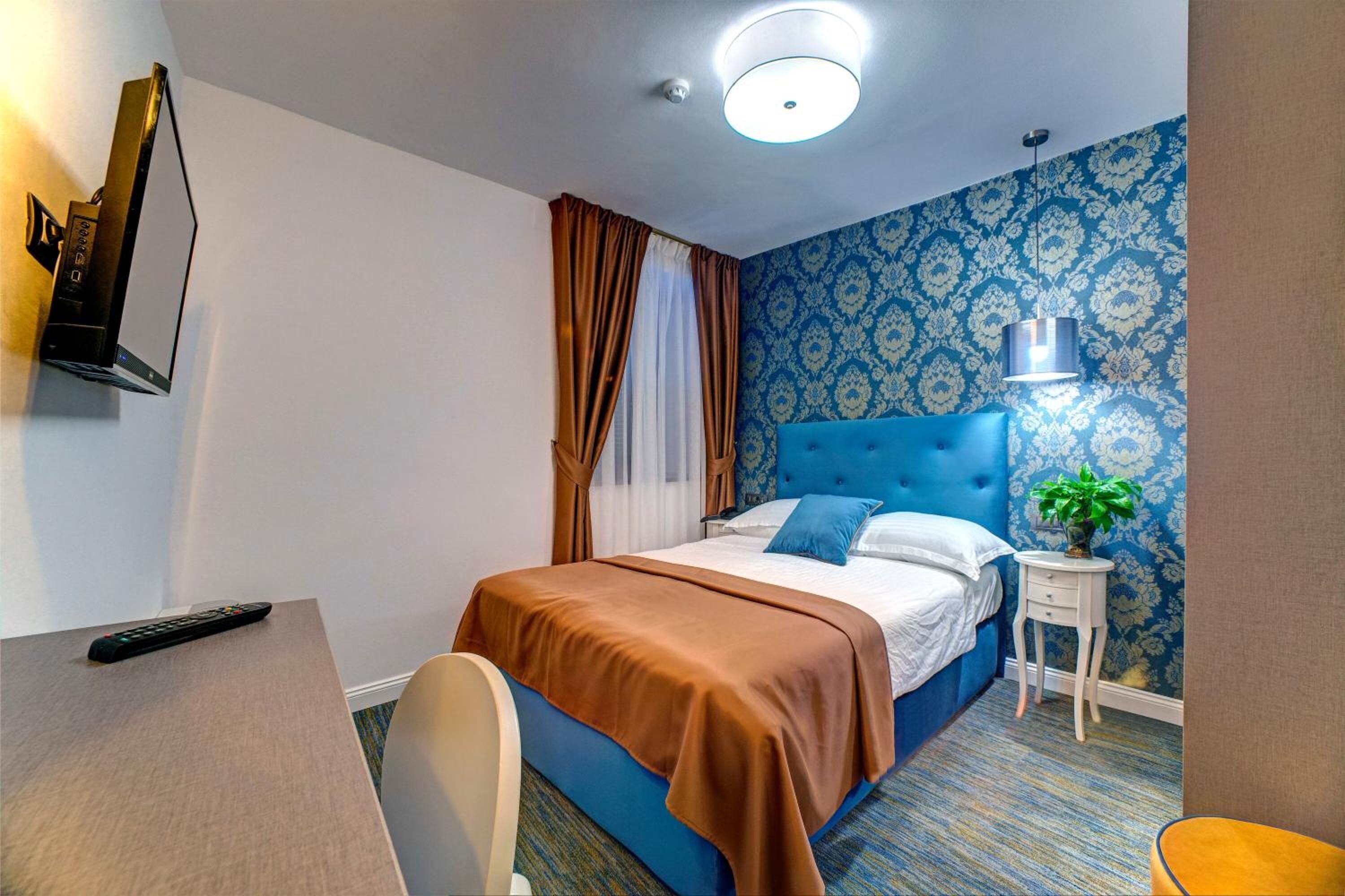 Habitación de hotel con cama, escritorio, silla, televisor, lámpara y planta.