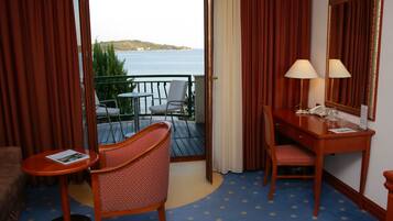 A hotel room with a balcony, a desk with a chair, a small table, and a mirror.