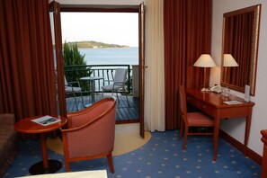 A hotel room with a balcony, a desk with a chair, a small table, and a mirror. - Hotel Villa Radin (Vodice)