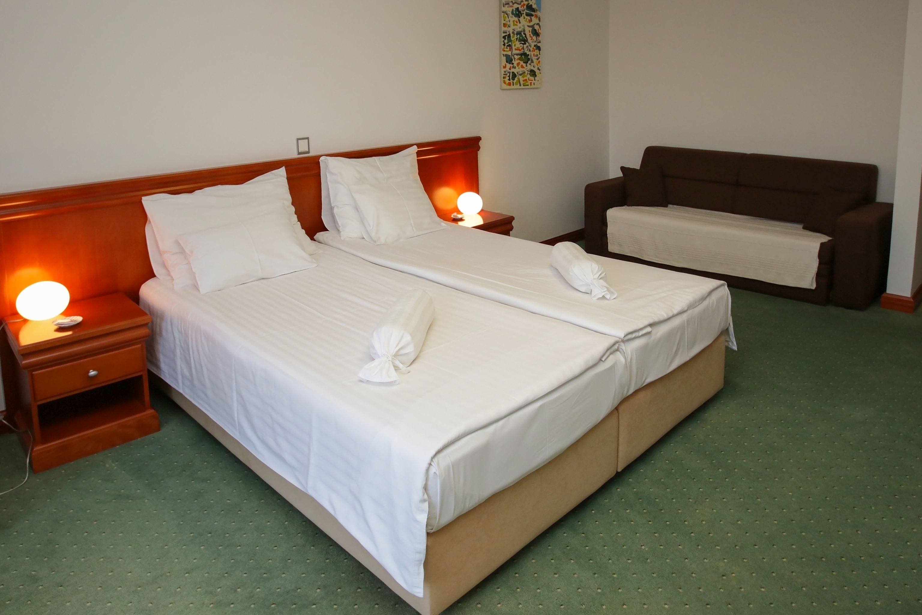 A hotel room with a large bed, two bedside tables with lamps, a brown sofa, and a green carpet.