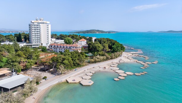 A coastal hotel with a large building labeled "PUNTA" and a beach with hexagonal stone platforms. - Hotel Villa Radin (Vodice)