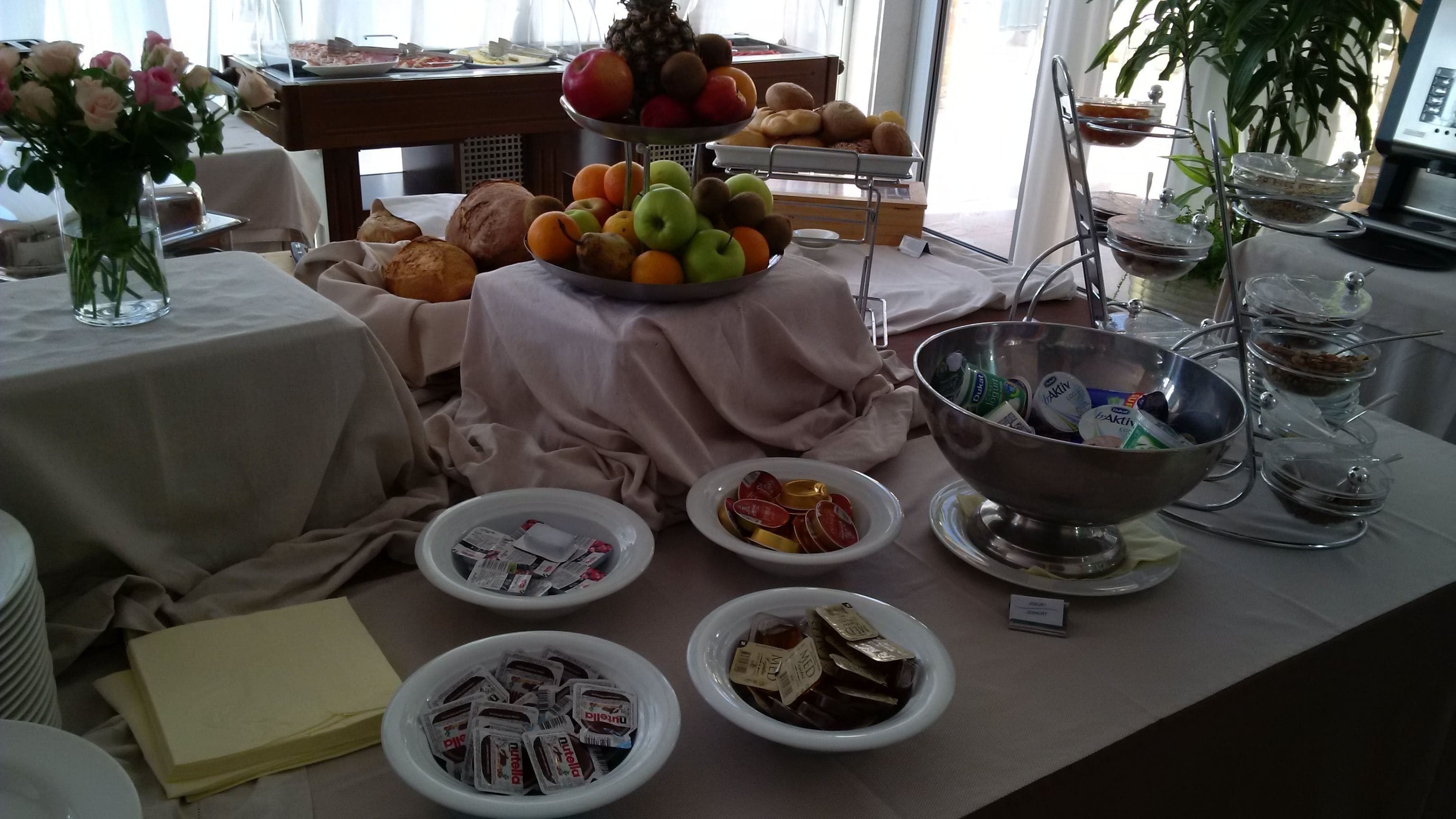 Una mesa de buffet con diversos alimentos, como frutas, pastelería y aperitivos envasados.