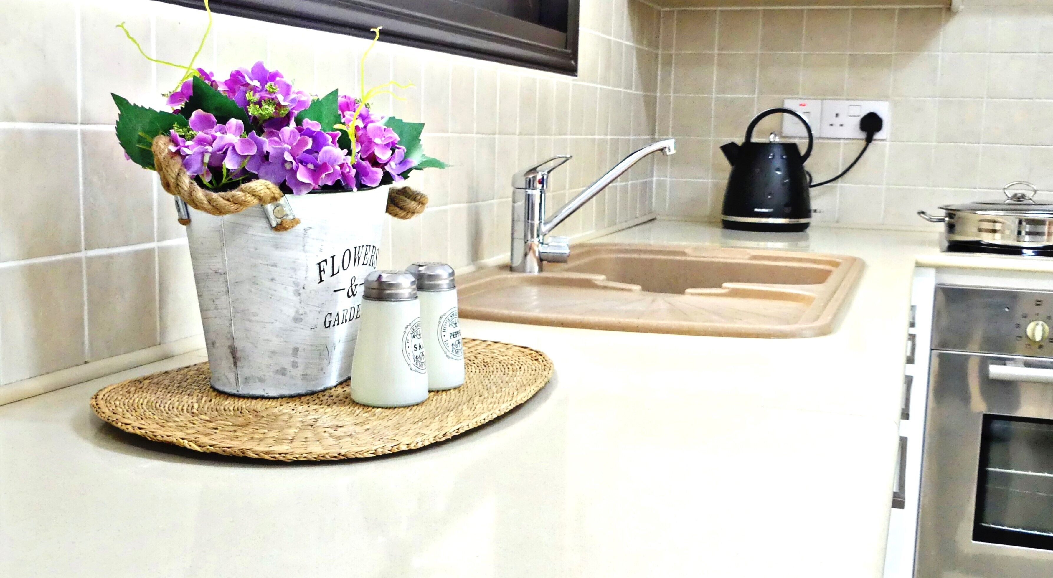 A kitchen with a sink, kettle, and a decorative flower pot on the counter.