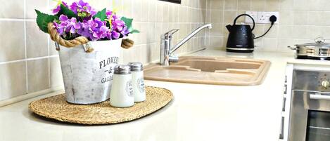 A kitchen with a sink, kettle, and a decorative flower pot on the counter.