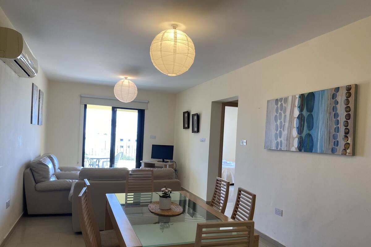 A modern living room with a sofa, a dining table with chairs, a TV, and artwork on the wall.