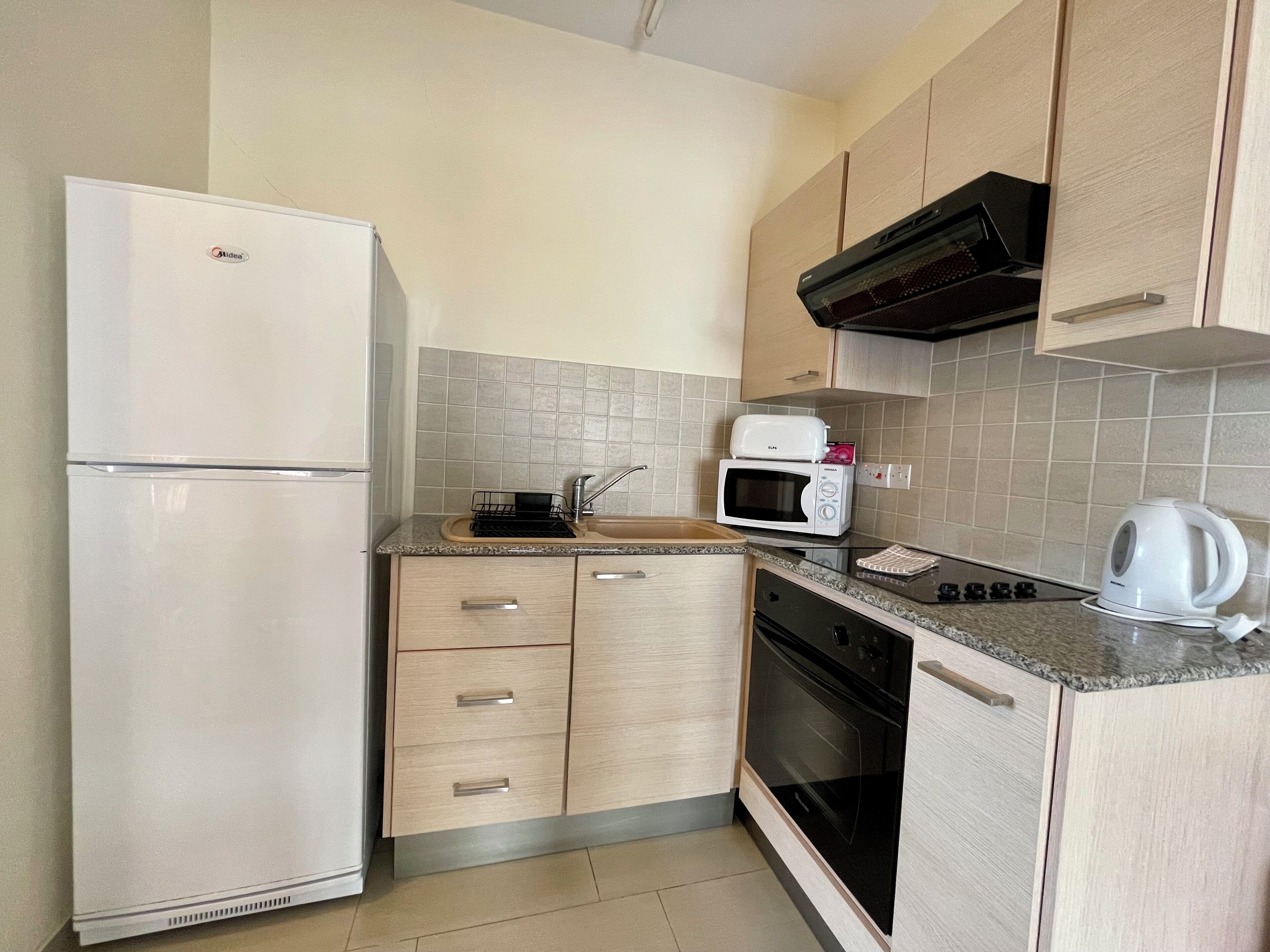 A compact kitchen with a refrigerator, microwave, oven, and a kettle.