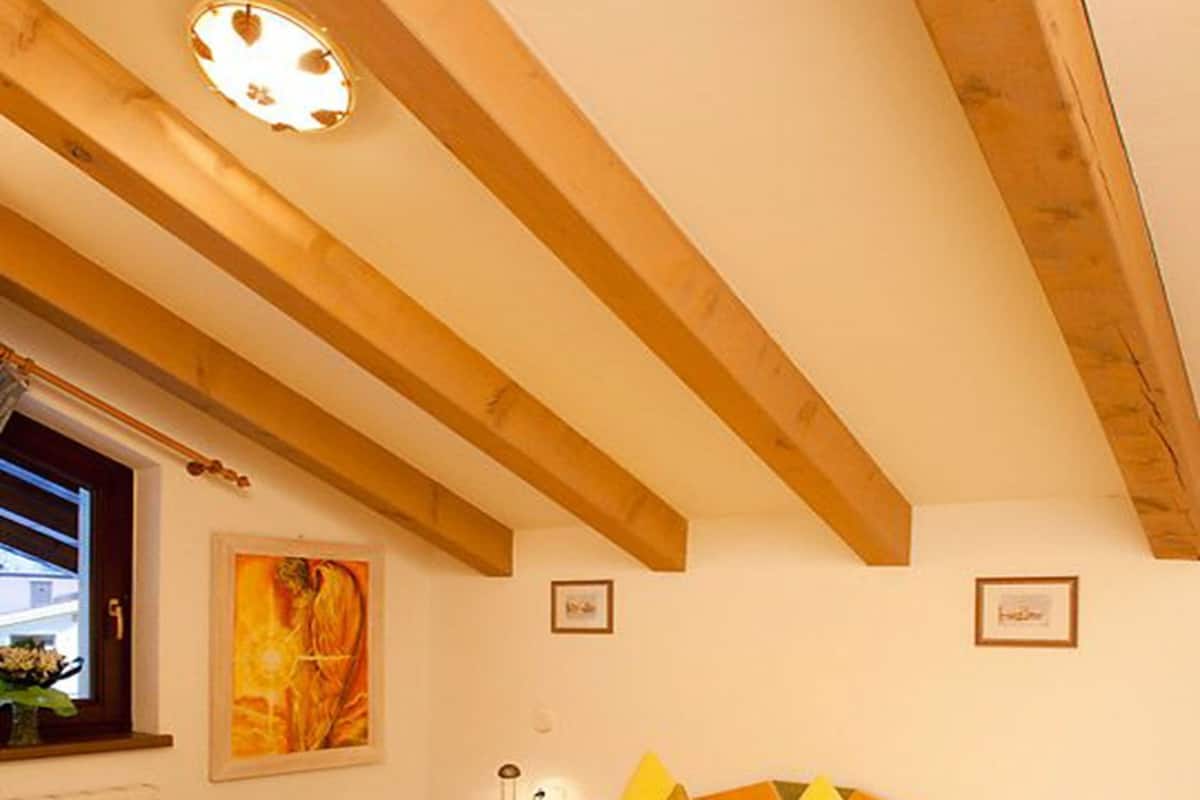 A room with a large bed, wooden beams on the ceiling, a window with a view, and a framed picture on the wall.