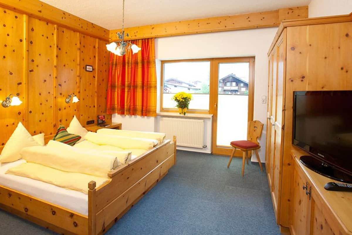 A wooden room with a bed, a TV, and a window with a view of a building.