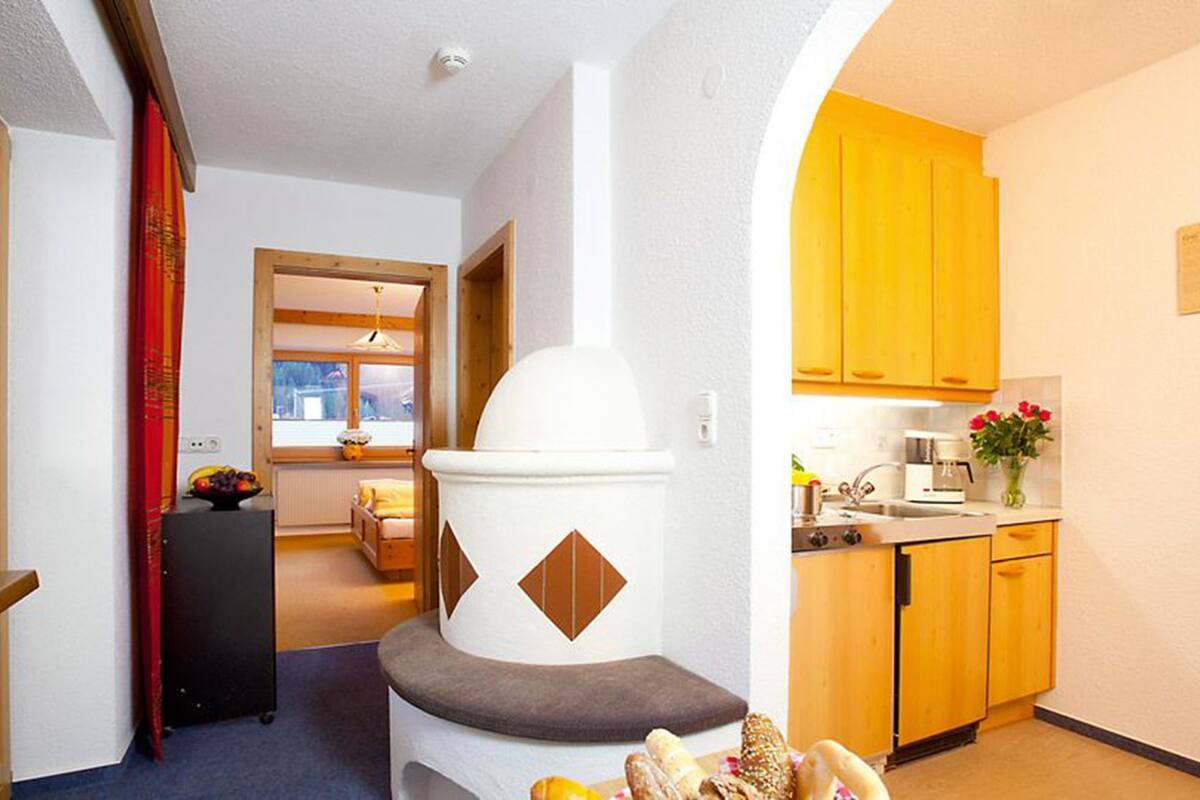 A compact kitchen with wooden cabinets, a white refrigerator, and a dining area visible through an open door.