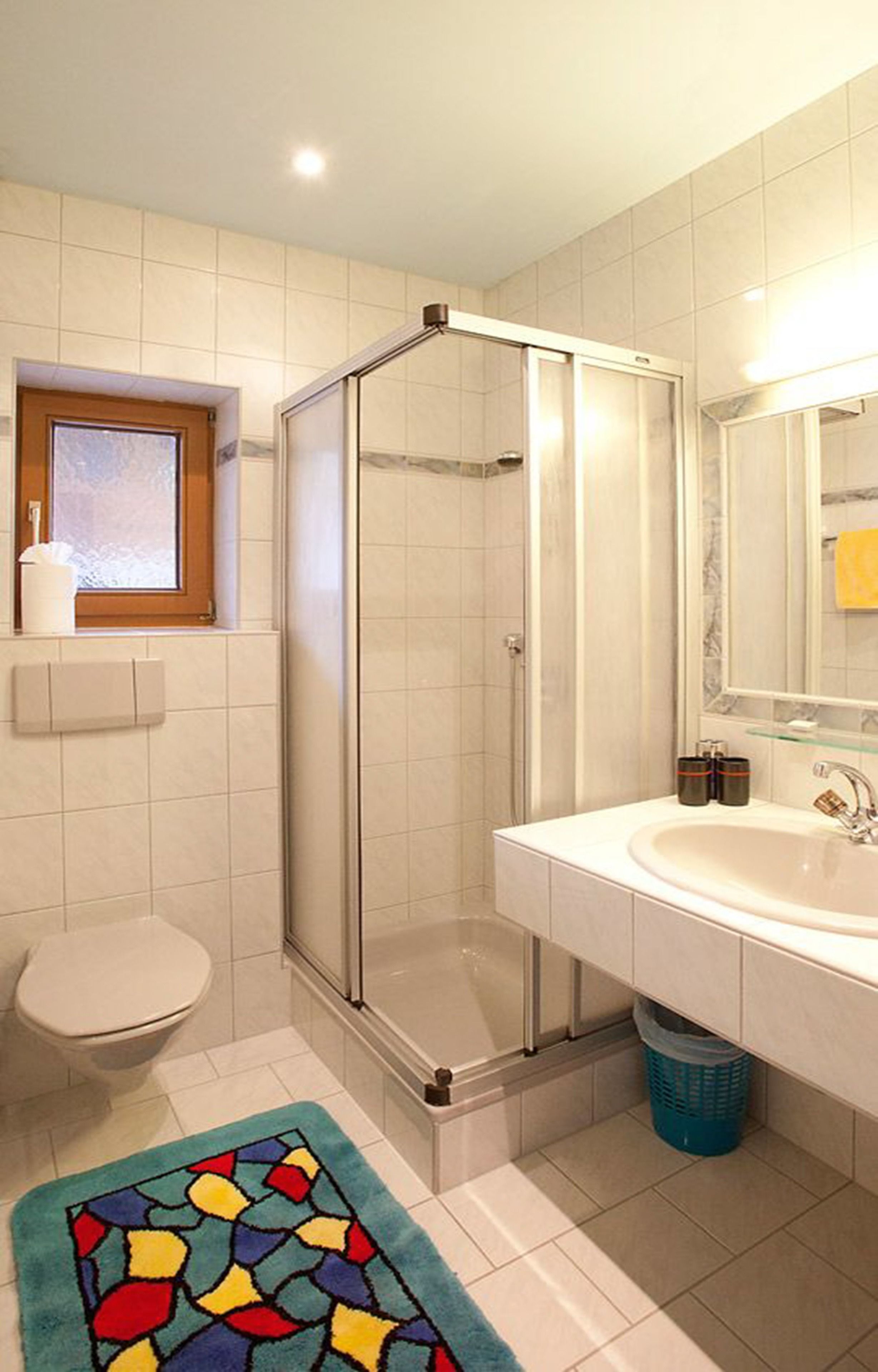 A bathroom with a shower enclosure, a toilet, a sink, and a window.
