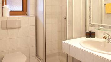 A bathroom with a shower enclosure, a toilet, a sink, and a window.