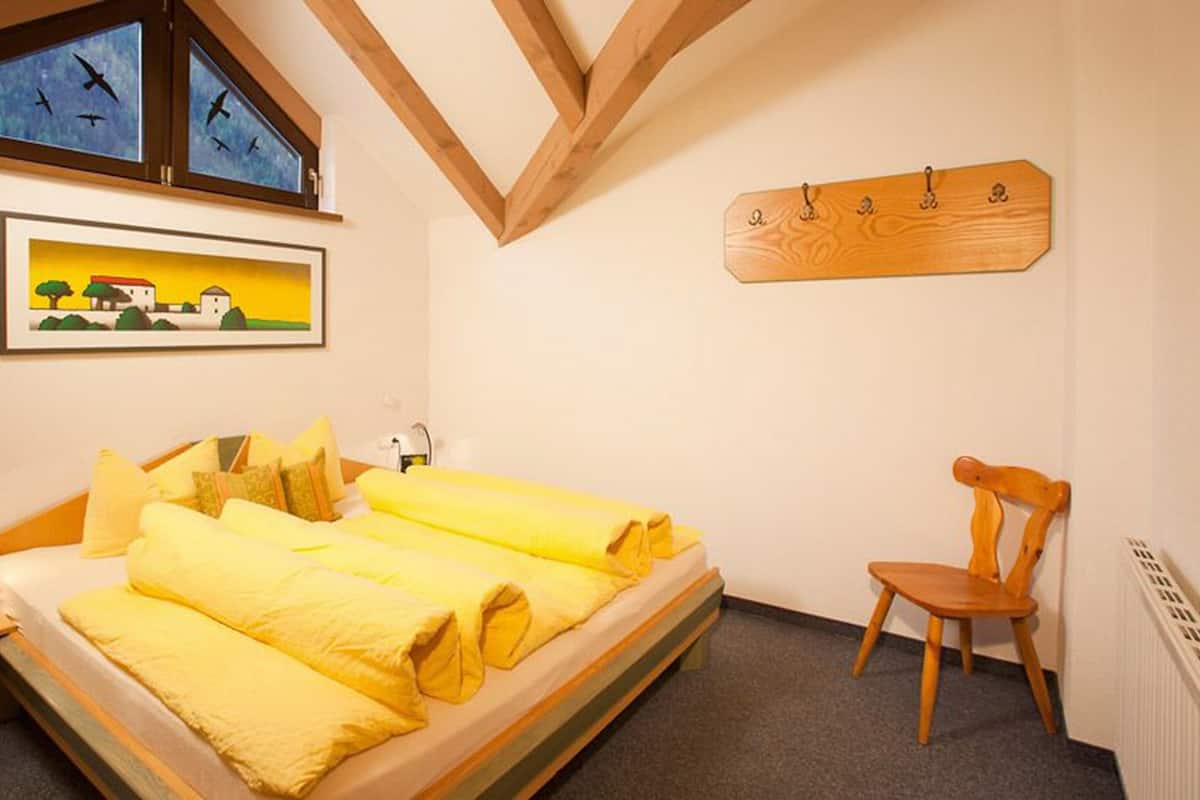 A bedroom with a bed, a chair, a desk, a clock, and a painting on the wall.