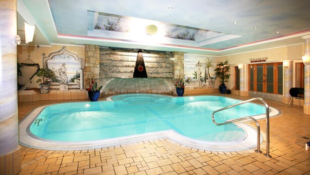 Una piscina interior con un fondo de pared de piedra, techo con tragaluces y un cartel que dice "TEPIDARIUM".