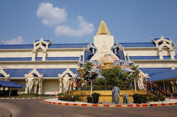 A large building with a blue roof, multiple statues, and colorful flags. - Savan Vegas Hotel & Casino (Savannakhet)