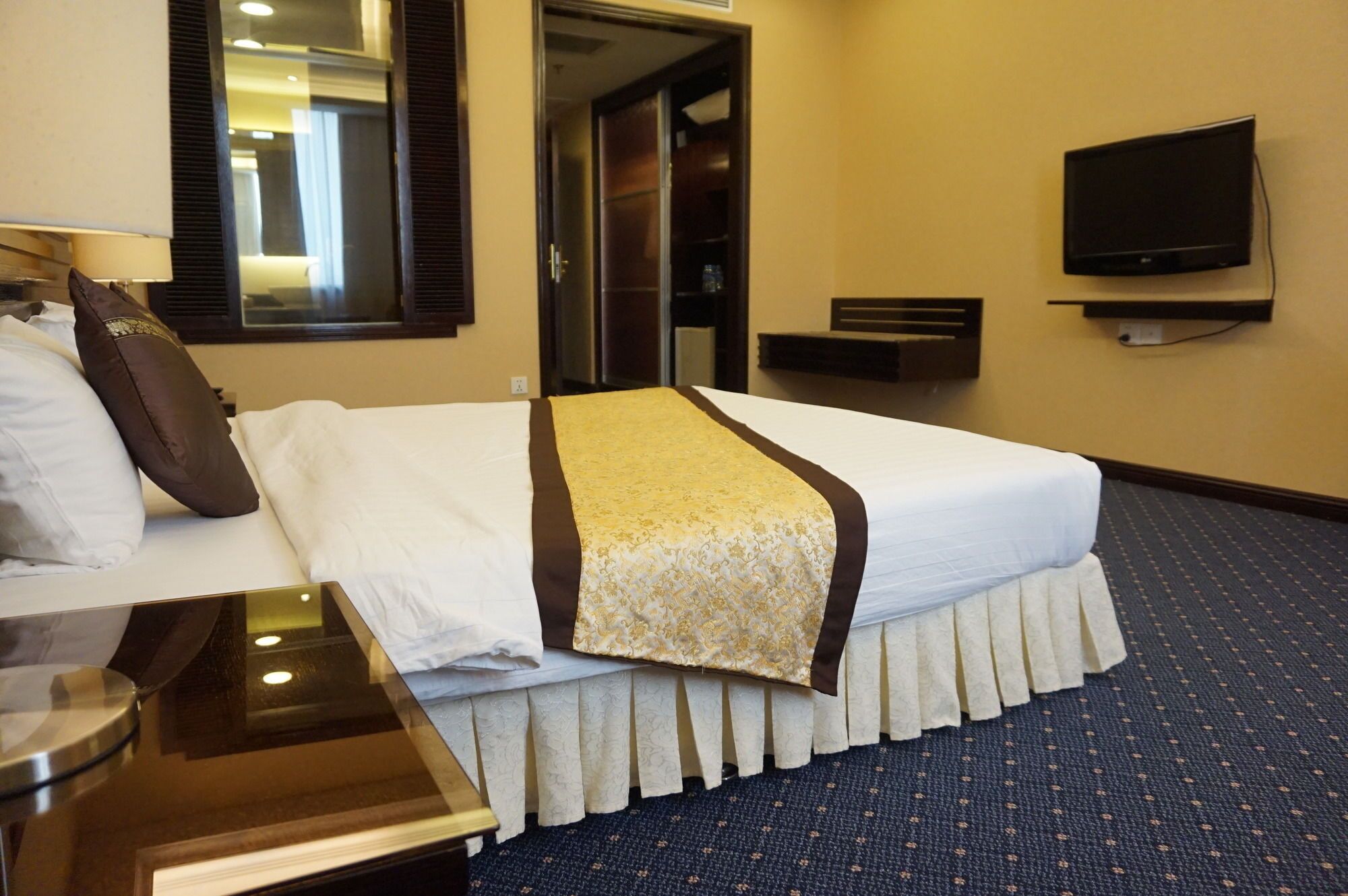 A hotel room with a bed, a bedside table, a lamp, a television, and a mirror.