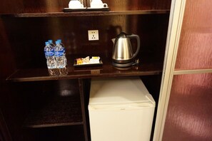 Une chambre d’hôtel équipée d’un mini-bar contenant deux bouteilles d’eau, d’un plateau avec des en-cas et d’une bouilloire électrique argentée.