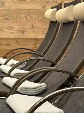A row of reclining chairs with grey fabric and metal frames, arranged against a wooden wall. - Aparthotel Garni Monte (Kartitsch)