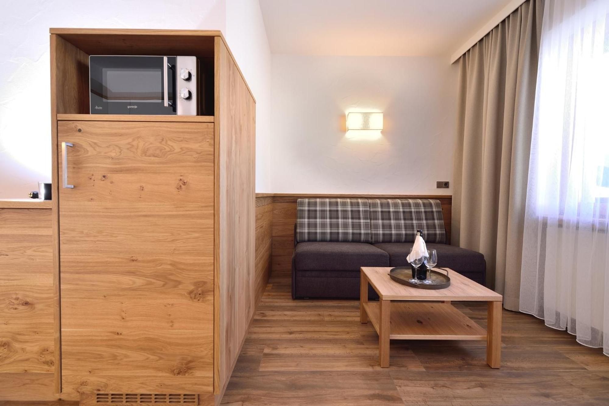 Habitación compacta con kitchenette, sofá, mesita y ventana con cortinas.