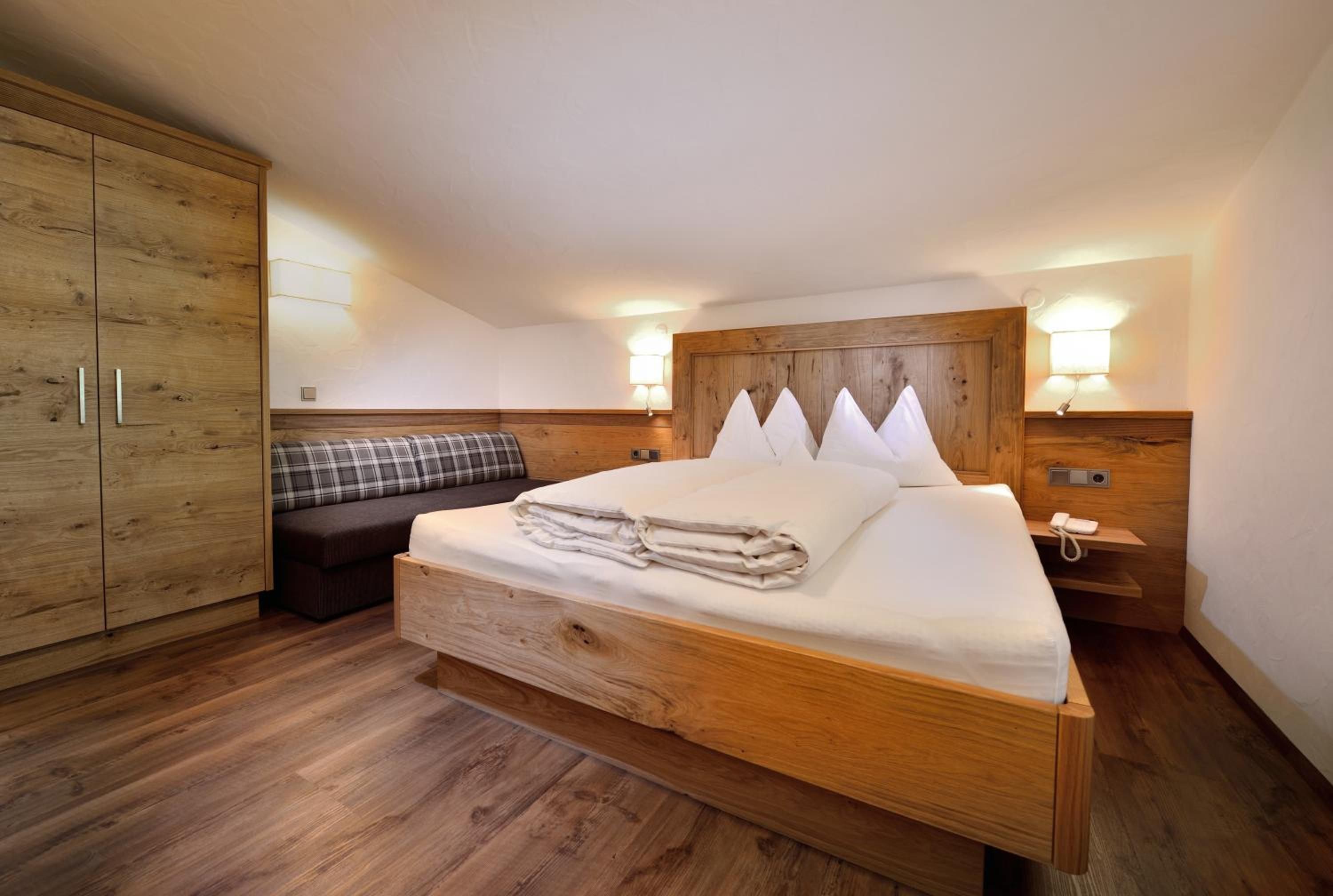 Un dormitorio con cama de madera, un banco, un armario y lámparas de noche.