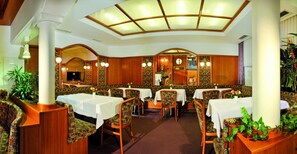 A restaurant with a high ceiling, patterned walls, and wooden furniture. Tables are set with white tablecloths and centerpieces. - Aparthotel Garni Monte (Kartitsch)