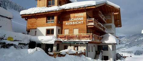 A wooden chalet hotel with a balcony and a sign reading 'Hotel Schöne Aussicht.'