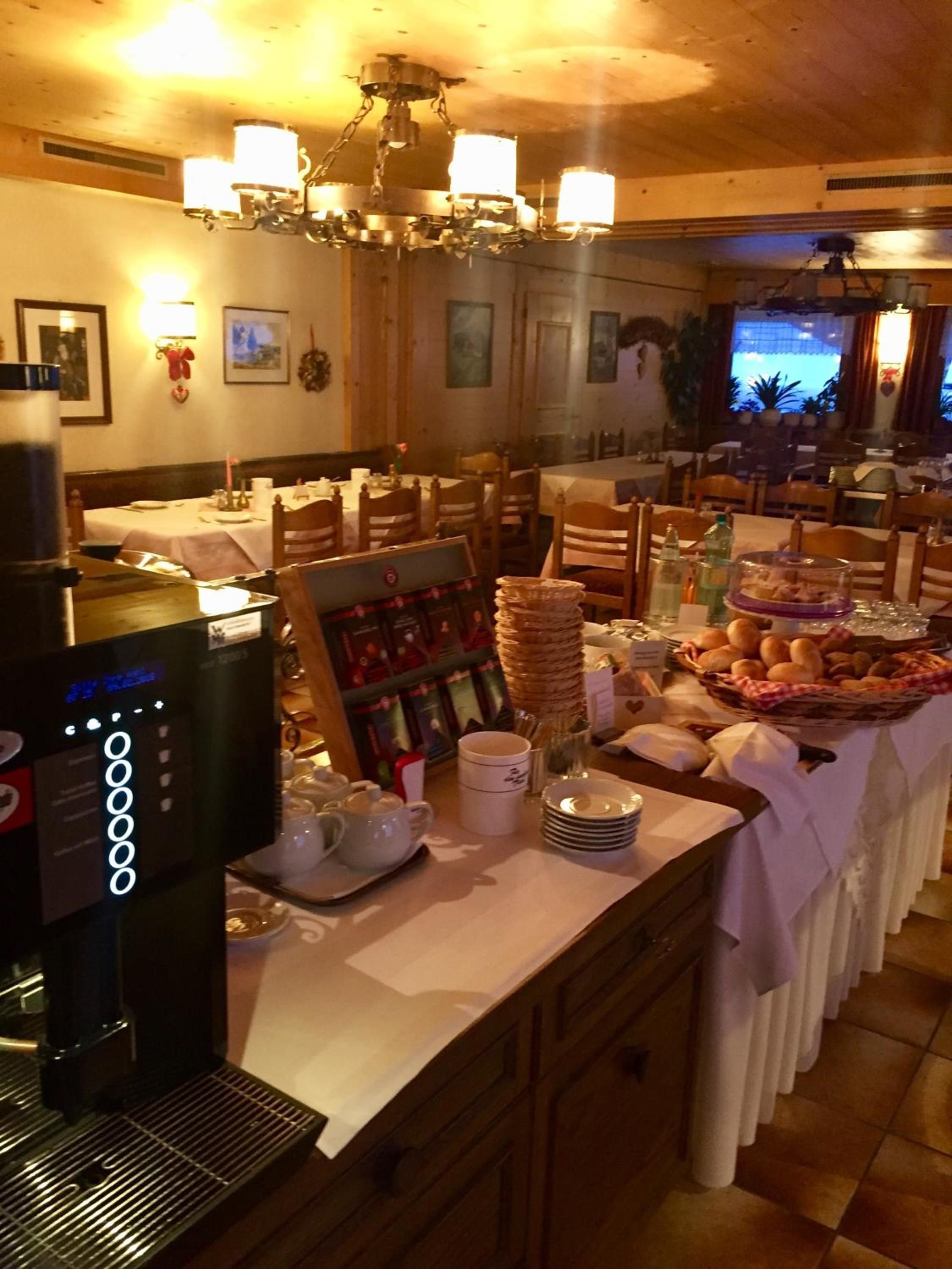 Montaje tipo bufé con una máquina de café, platos, tazones y una variedad de alimentos sobre una mesa.