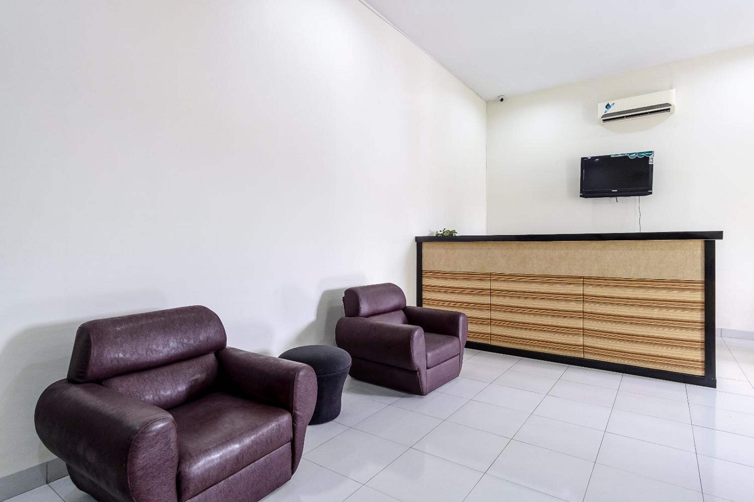 Un espace d’accueil comprenant un comptoir de réception, deux fauteuils en cuir, un petit pouf rond et un téléviseur à écran plat fixé au mur.