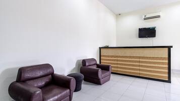 Un espace d’accueil comprenant un comptoir de réception, deux fauteuils en cuir, un petit pouf rond et un téléviseur à écran plat fixé au mur.