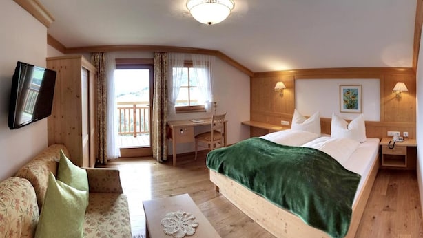 Una habitación de hotel con cama, escritorio, silla, televisor y balcón.