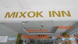 L’extérieur du Mixok INN, avec une enseigne bien visible indiquant : « Bienvenue au Mixok INN ».