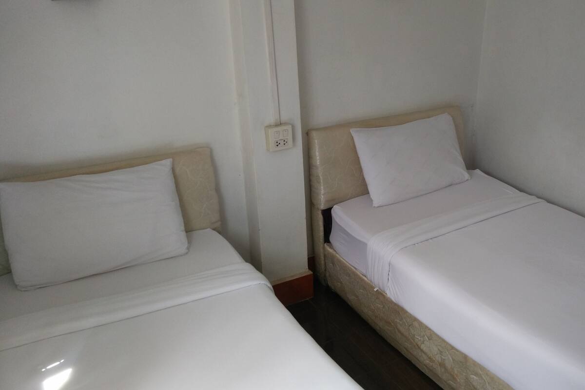 Two single beds with wooden headboards and white bedding in a room with plain walls and a visible electrical outlet.