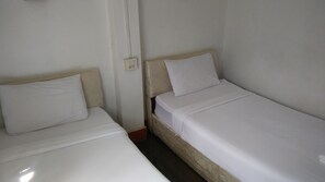 Two single beds with wooden headboards and white bedding in a room with plain walls and a visible electrical outlet. - Mixok Inn (Vientiane)