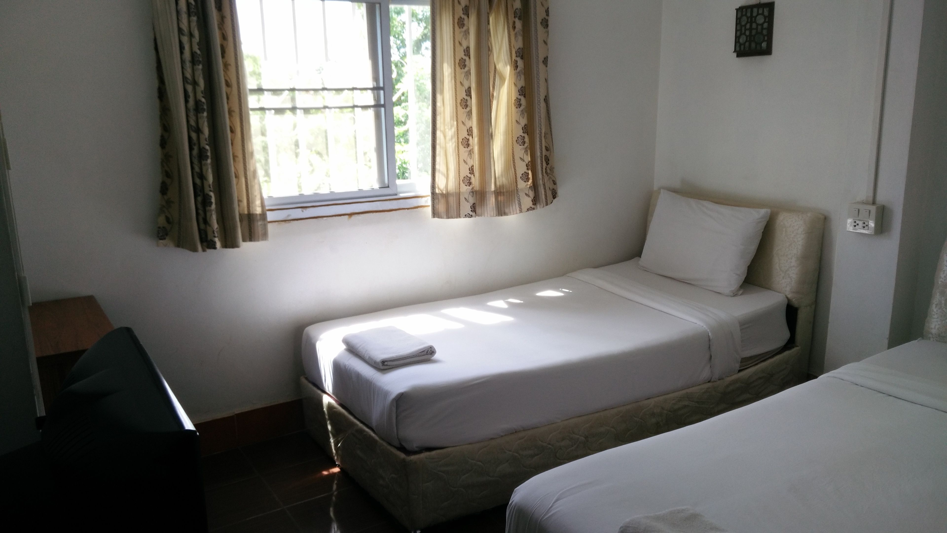 Una habitación pequeña con cama individual, ventana, escritorio y toma de corriente en la pared.
