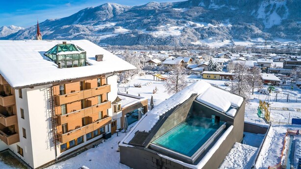 A hotel with a glass-enclosed pool, snow-covered surroundings, and a mountain backdrop. - Hotel Schwarzbrunn Superior (Stans)