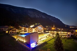 A large, well-lit hotel with multiple buildings, a swimming pool, and a mountainous backdrop. - Hotel Schwarzbrunn Superior (Stans)