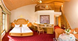 A hotel room with a large bed, a desk, a chair, and a staircase leading to an upper level. - Hotel Schwarzbrunn Superior (Stans)