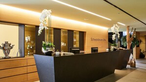 A reception desk with a modern design, a wooden counter, and a sign that reads "Schwarzwald SPA". - Hotel Schwarzbrunn Superior (Stans)