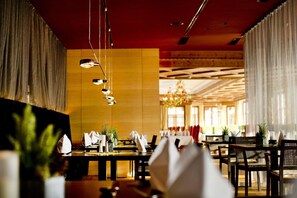 A restaurant with multiple tables, hanging lights, and a large chandelier. - Hotel Schwarzbrunn Superior (Stans)